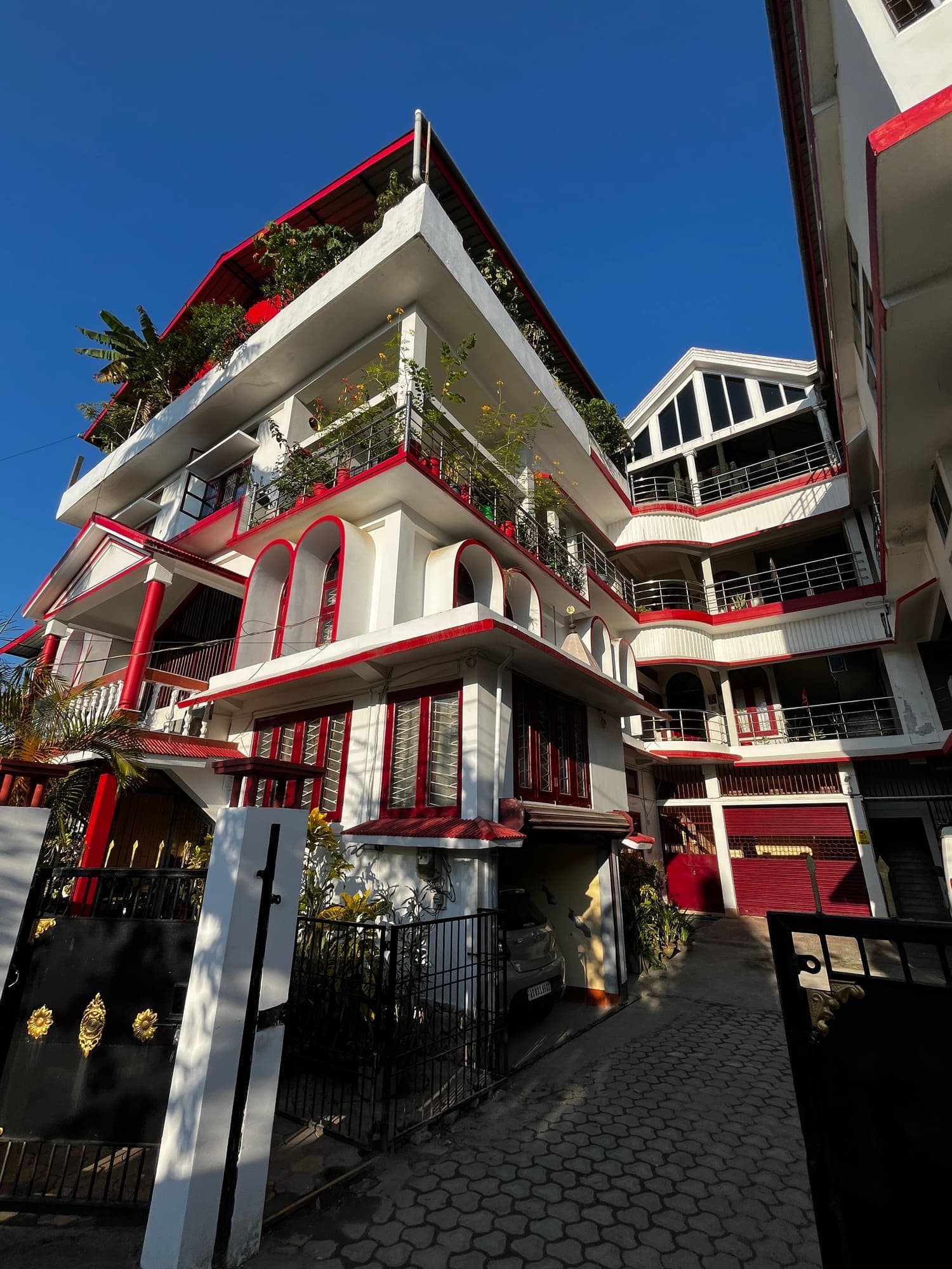 The Birdhouse Homestay's white and red building with plant-filled balconies, seen from the front gate